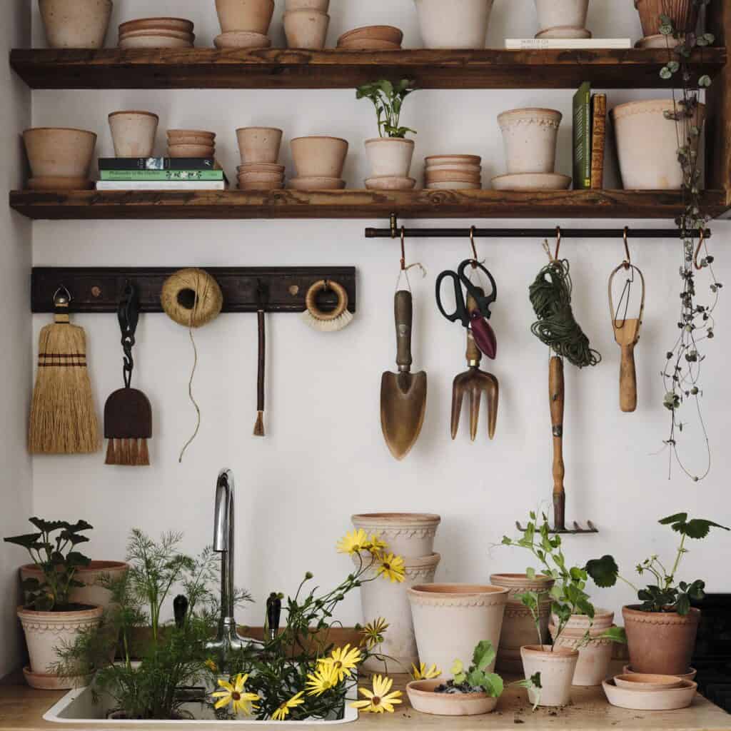 Inomhusbild av en trädgårdsverkstad med hyllor fyllda med Helena krukor i terrakotta från Bergs Potter, tillsammans med trädgårdsverktyg och växter.
