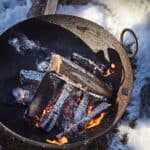 Eldkorg i järn med sprakande eld utomhus i vintermiljö.