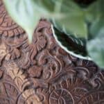 Närbild av ett sidobord i trä från Dutchbone med ett detaljerat och snirkligt mönster på bordsskivan, tillsammans med en grön krukväxt i en keramikskål.