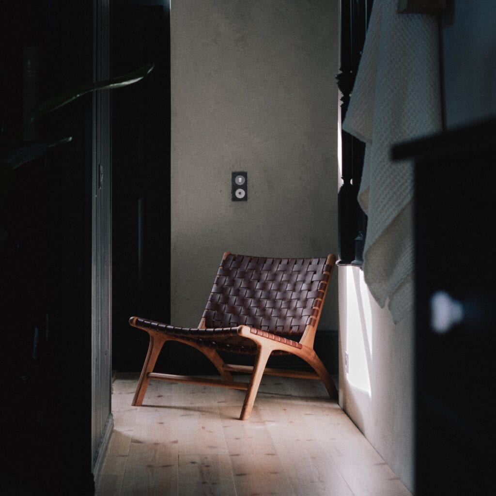 Porto fåtölj stor i teak och flätat läder i konjakston placerad i lugn inomhusmiljö