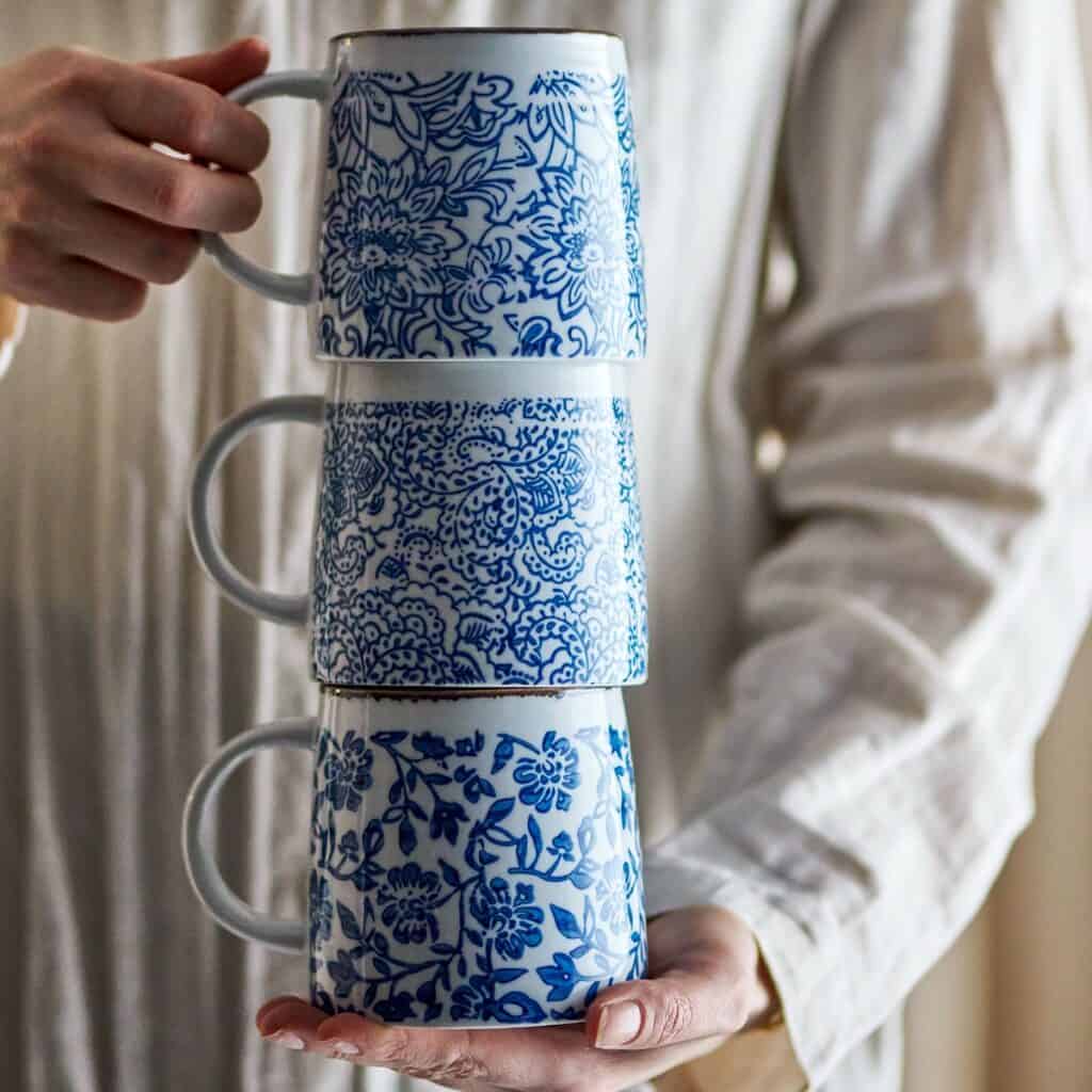 Tre blåvita Molly-muggar i stengods med olika blommönster staplade i händer