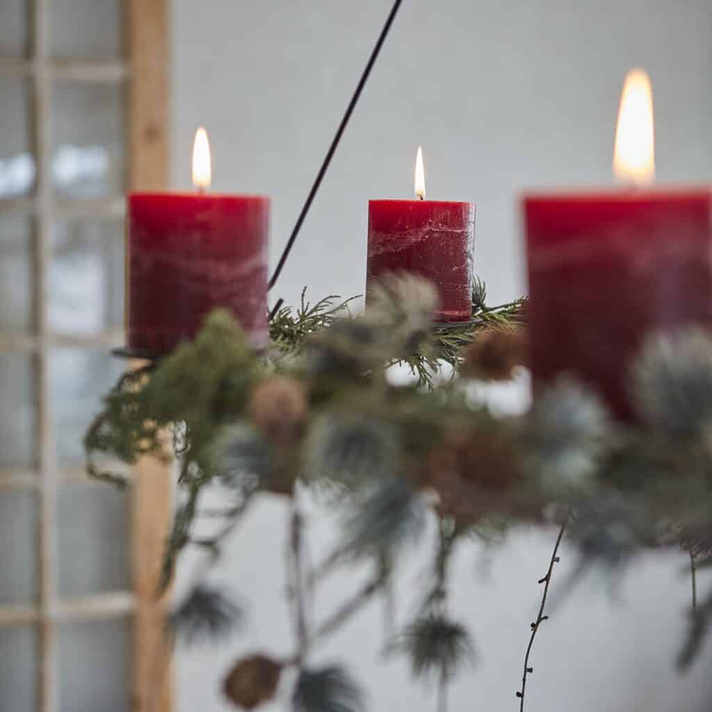 AXEL takkrona dekorerad med röda blockljus och gröna kvistar för julstämning.