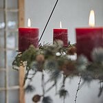 AXEL takkrona dekorerad med röda blockljus och gröna kvistar för julstämning.