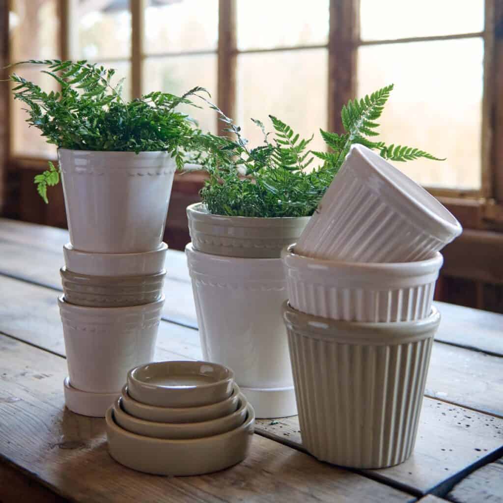 Vita blomkrukor ASTRID med fat och gröna växter på träbord vid fönster