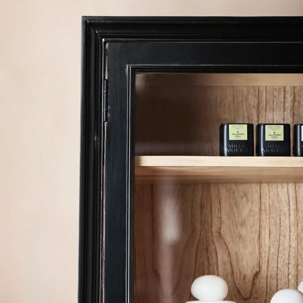 Detaljbild på övre hörnet av vitrinskåpet VIVA från Nordal, med svart ram, glas och trädetaljer inuti.