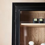 Detaljbild på övre hörnet av vitrinskåpet VIVA från Nordal, med svart ram, glas och trädetaljer inuti.