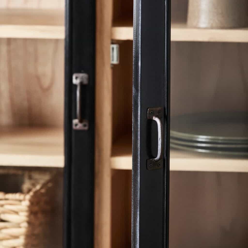 Närbild på handtagen och glasdörrarna på vitrinskåpet VIVA från Nordal, med inblick i trähyllorna och porslin.