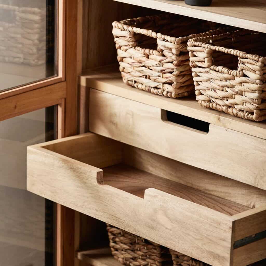 Närbild på en öppen låda och hyllor med flätade korgar i vitrinskåpet VIVA från Nordal, med glasdörrar och trädetaljer.