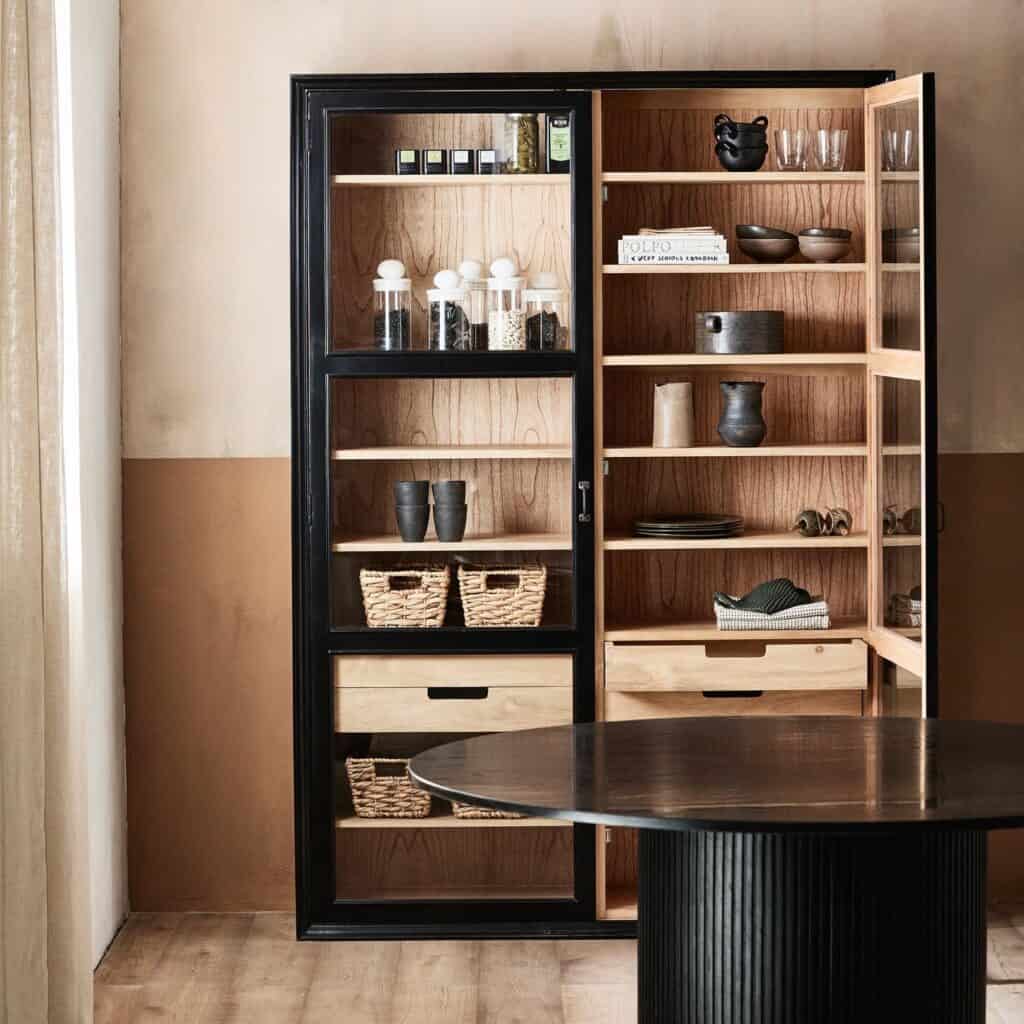 Vitrinskåp VIVA från Nordal med glasdörrar, öppna dörrar och hyllor fyllda med förvaringsdetaljer som korgar och porslin, i en stilren miljö med naturliga färger.