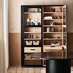 Vitrinskåp VIVA från Nordal med glasdörrar, öppna dörrar och hyllor fyllda med förvaringsdetaljer som korgar och porslin, i en stilren miljö med naturliga färger.