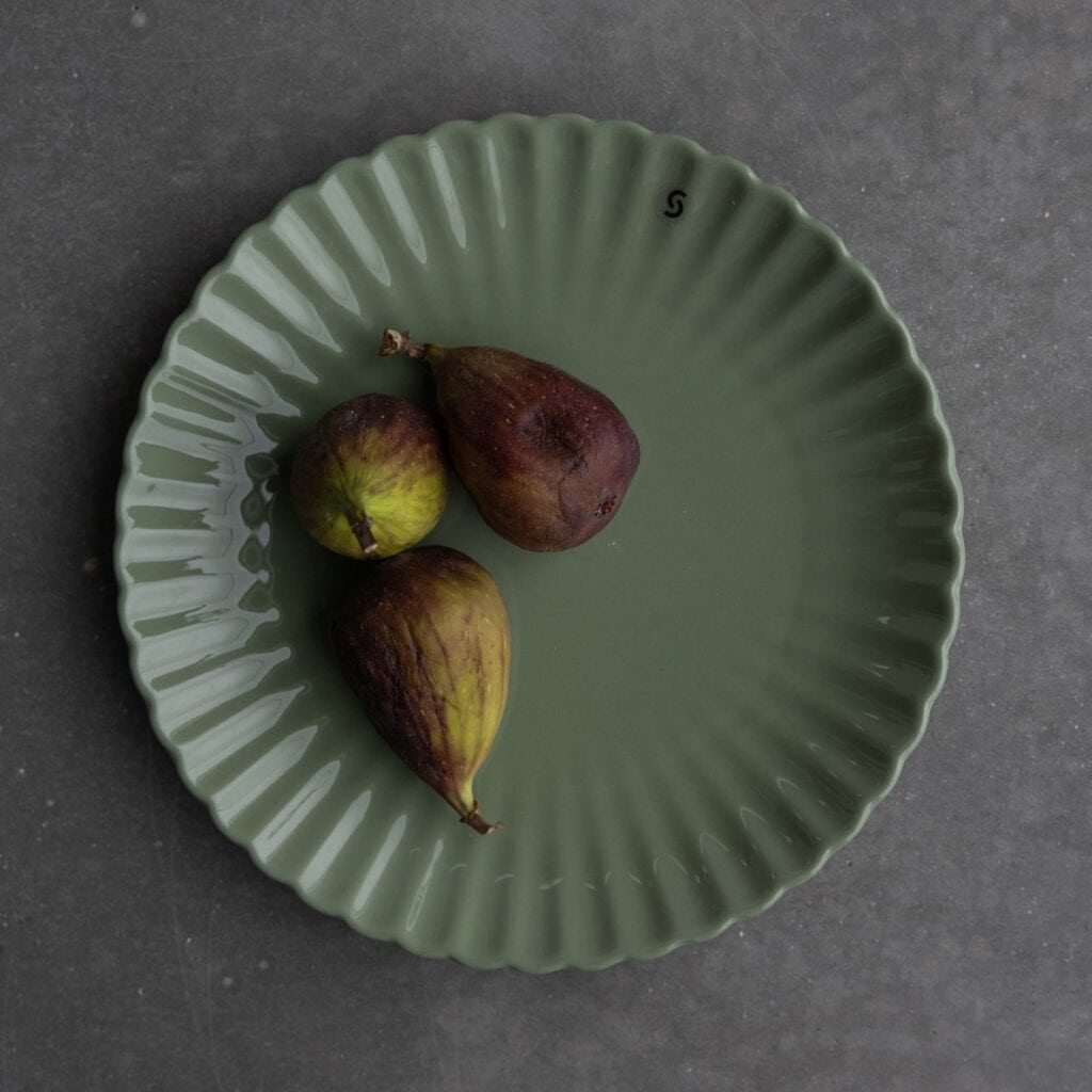 Grön assiett FLORA från varumärket Storefactory, dekorerad med fikon och placerad på en grå yta.