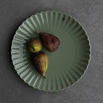 Grön assiett FLORA från varumärket Storefactory, dekorerad med fikon och placerad på en grå yta.