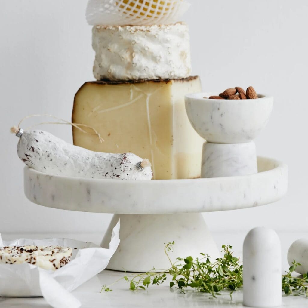 Kakfat i vit marmor från Nordal med ost, chark och mandlar – perfekt för servering.