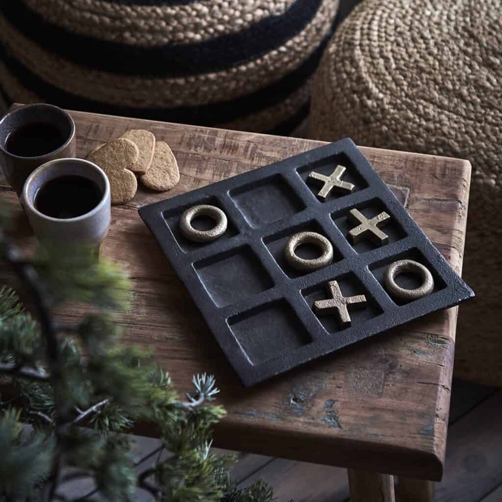 Luffarschack GLOBETROTTER i järn från Affari of Sweden i svart och guldfärg, placerat på ett rustikt träbord med kaffekoppar och pepparkakor i bakgrunden.