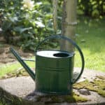 Grön vattenkanna i metall – klassisk och hållbar design för trädgården, placerad vid gammaldags vattenpump.