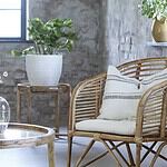 Bali brickbord i naturligt trä med vävd rottingbricka, placerat i ett rustikt vardagsrum tillsammans med en rottingfåtölj och krukväxt.