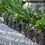 Ett dekorativt kantskydd i gjutjärn från Esschert Design som avgränsar en grusgång från en grönskande rabatt med växter.