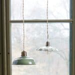 Taklampa Gustav Vit i vågigt glas och mässing hängande i köksfönster med grön växt och keramik.
