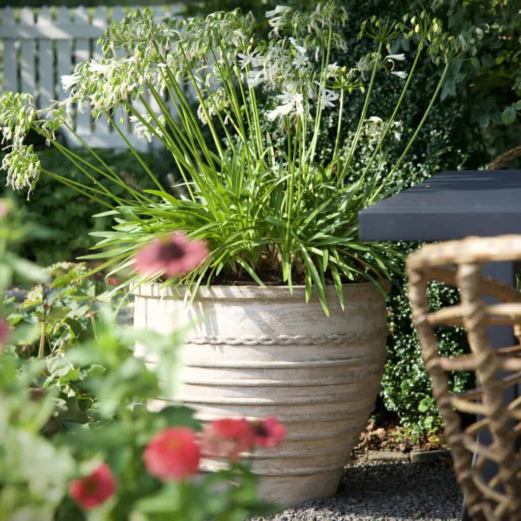 Terrakottakruka TALIA från Wikholm Form, en stor handgjord kruka i klassisk design, placerad i trädgårdsmiljö med blommande växter.