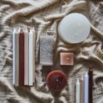 Miljöbild med blandade paraffinljus i olika färger och former på ett naturfärgat tyg.