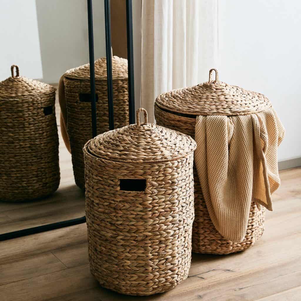 Tvättkorgar Cosna från Nordal i vattenhyacint med handtag och lock, vackert placerade i en inomhusmiljö.
