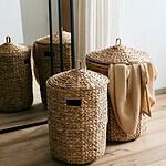 Tvättkorgar Cosna från Nordal i vattenhyacint med handtag och lock, vackert placerade i en inomhusmiljö.