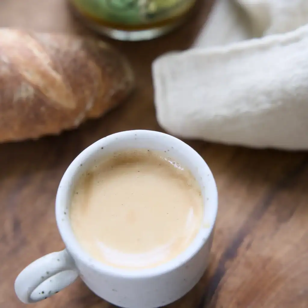 En espressomugg från Nordal, modell GRAINY, fylld med nybryggd espresso. Muggen står på ett träbord bredvid ett bröd och en tygservett.