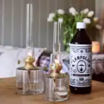 Strömshagas lampolja står bredvid två tända fotogenlampor i glas och mässing på ett träbord.