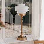 VALTER bordslampa från Strömshaga i mässing med vit opalglas skärm placerad på ett fönsterbräde.