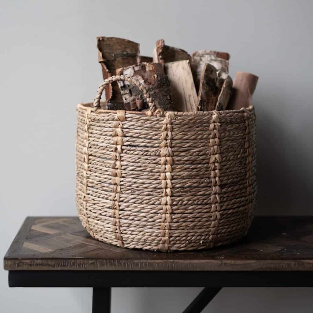 Korg i naturlig rotting med ved, modell CARLA från Wikholm Form, placerad på ett rustikt träbord mot en neutral bakgrund.