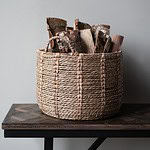 Korg i naturlig rotting med ved, modell CARLA från Wikholm Form, placerad på ett rustikt träbord mot en neutral bakgrund.