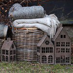 Tre dekorationshus i rostad metall placerade utomhus framför en korg med filtar, perfekt för att skapa en mysig och rustik atmosfär i trädgården eller på uteplatsen.