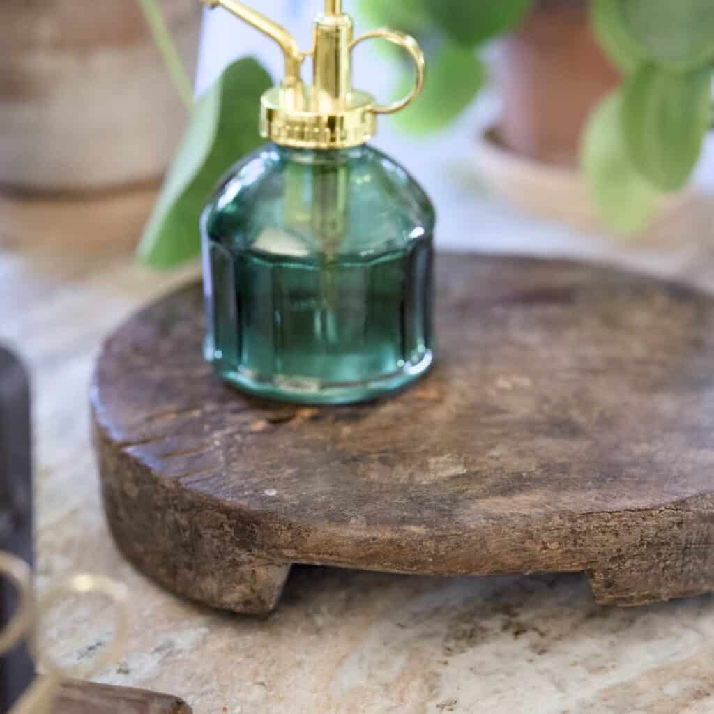 Rustik rund bricka i återvunnet trä med naturlig patina, placerad på en marmoryta. På brickan står en grön glasblomspruta med gulddetaljer.