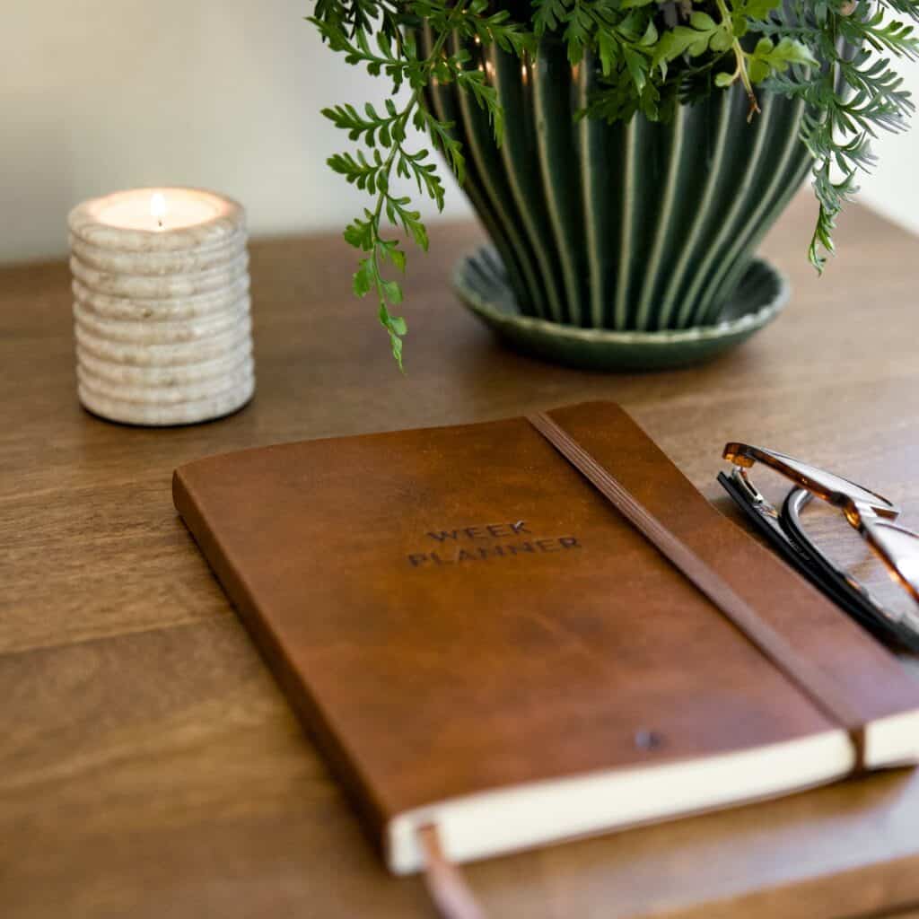 Konsolbord BETTON i mangotra med anteckningsbok, glasogon, ljus och gron vas – detaljbild i varm hemmiljo.