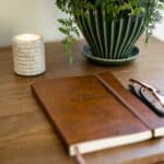 Konsolbord BETTON i mangotra med anteckningsbok, glasogon, ljus och gron vas – detaljbild i varm hemmiljo.