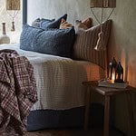 En mysigt inredd sovrumsmiljö med säng klädd i mjuka textilier och kuddar i jordnära toner. På nattduksbordet står lyktan GIZA från Affari of Sweden, tänd för att skapa en varm och stämningsfull atmosfär.