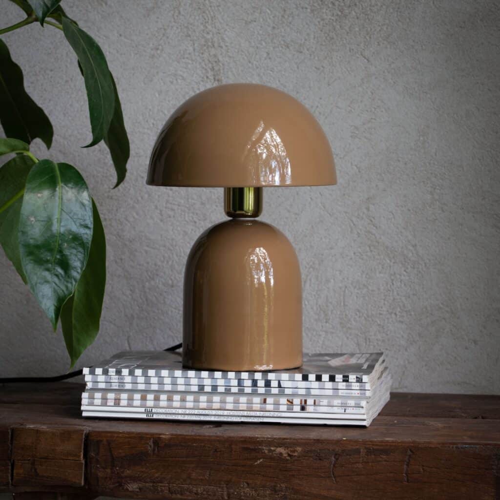 Brun bordslampa ROME från Wikholm Form, placerad på en hög med böcker på ett rustikt träbord, med en grön växt i bakgrunden.