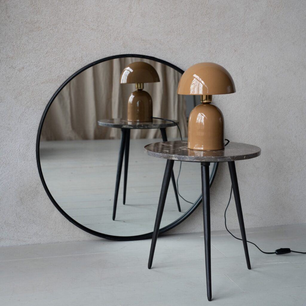 Brun bordslampa ROME från Wikholm Form, placerad på en hög med böcker på ett rustikt träbord, med en grön växt i bakgrunden.