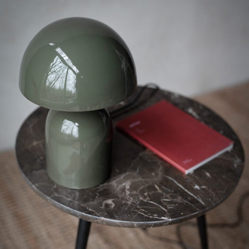 Grön bordslampa ROME från Wikholm Form, placerad på ett runt marmorbord bredvid en röd anteckningsbok.