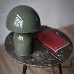 Grön bordslampa ROME från Wikholm Form, placerad på ett runt marmorbord bredvid en röd anteckningsbok.