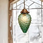 Närbild på Taklampa DRUVA från Strömshaga, tänd, med en grön glasskärm och mässingsfäste framför ett fönster.