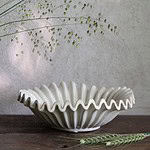 Vitmelerat stengodsfat HANNA från Wikholm Form, placerat på ett rustikt träbord med dekorativa gröna kvistar.