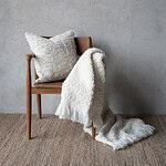 Offwhite pläd NALIA från Wikholm Form, draperad över en trästol tillsammans med ett matchande kuddfodral, mot en neutral vägg.