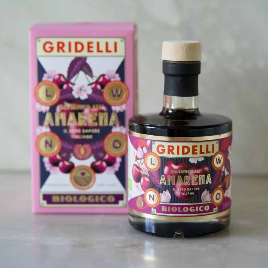 Flaska med Gridelli Balsamico Amarena bredvid dess färgglada förpackning på ett marmorbord.