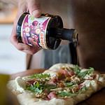 En person häller Gridelli Balsamico Amarena över en pizza toppad med ruccola, prosciutto och valnötter.