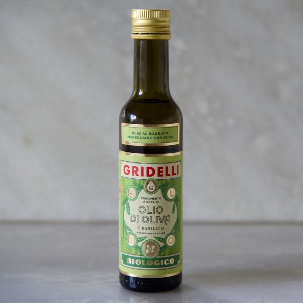 Flaska av Gridelli ekologisk olivolja med smak av basilika, fotograferad på en marmoryta.