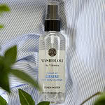 Washologi linnevatten Desire med doft av bomullsblomma, placerad på ett randigt blått tyg med gröna växter i förgrunden.