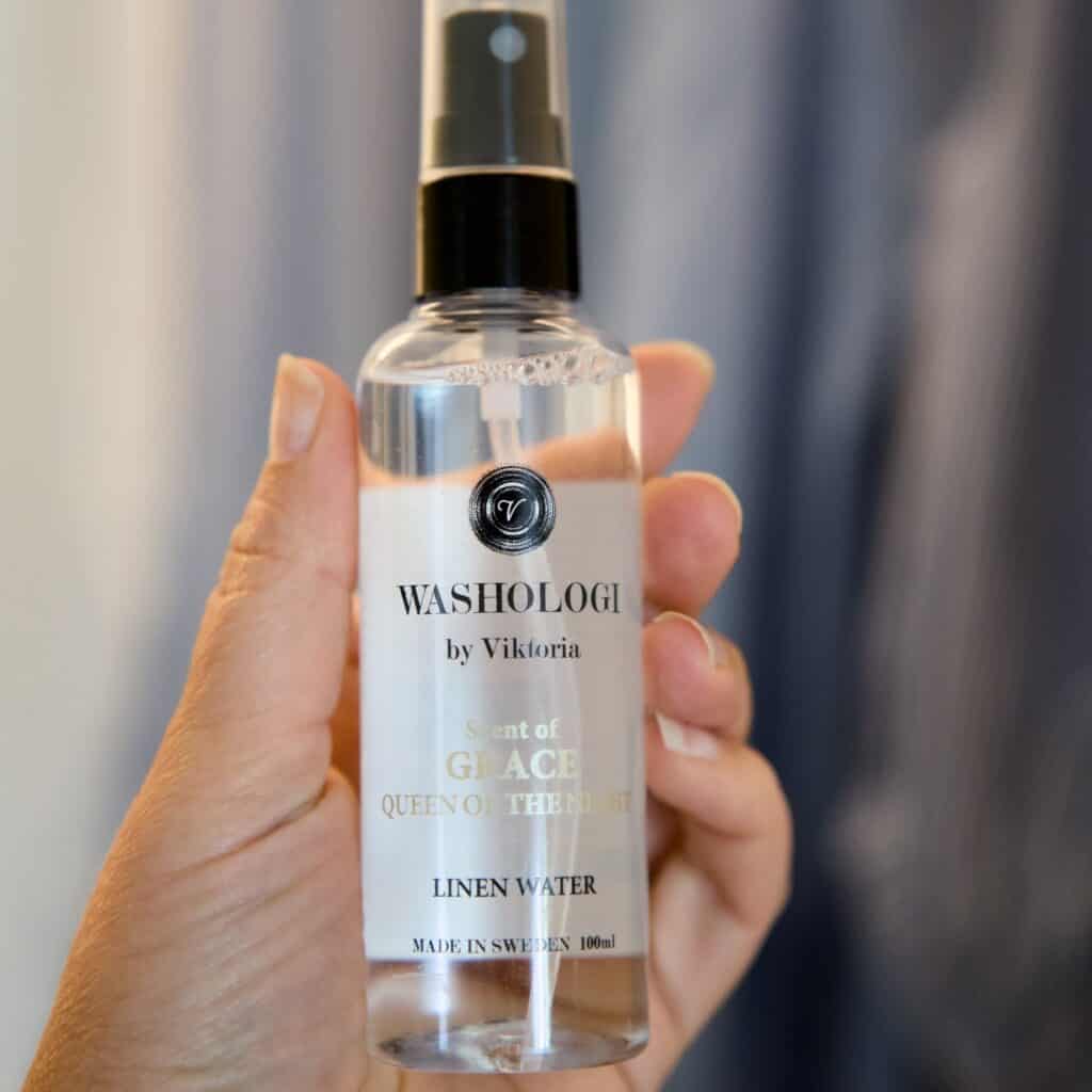 Hand som håller en flaska Washologi linnevatten Grace, med en förtrollande doft av nattens drottning.