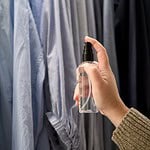 Hand som sprayar Washologi linnevatten Grace på kläder i en garderob.