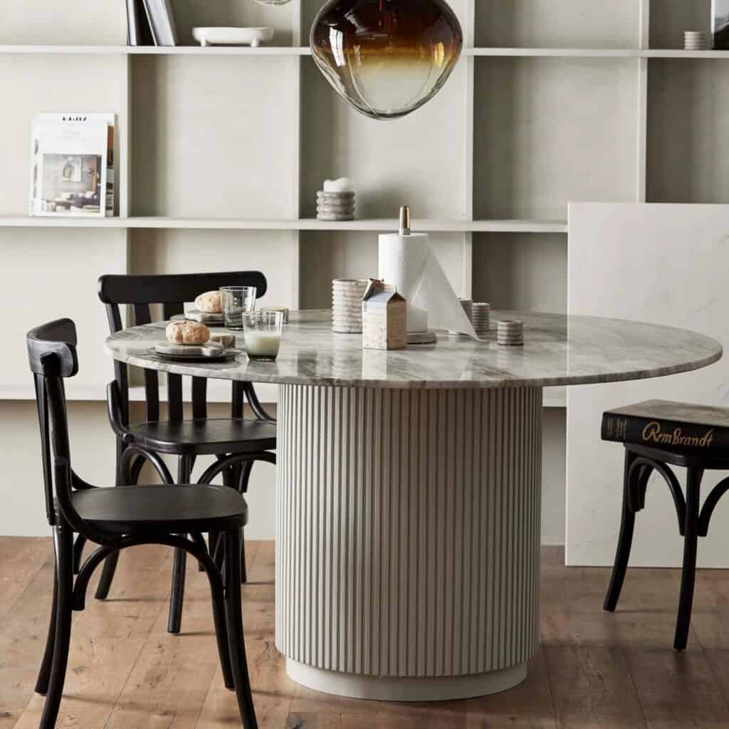 ERIE matbord uppställt i en matsal med bokhyllor i bakgrunden och svarta trästolar runt bordet, dekorerat med en lampa och frukosttillbehör.